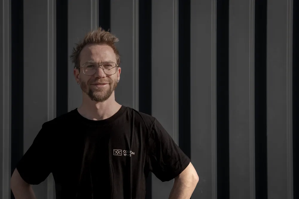 Ferdinand steht vor eine dunklen Wand und blickt gelassen in die Kamera